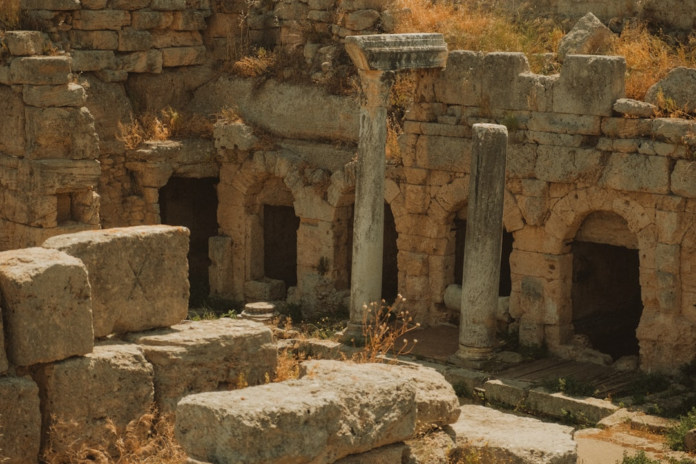 Sun-drenched ancient stone ruins, featuring arched doorways, crumbling columns, and scattered blocks, evoke the enduring mysteries of a past civilization.