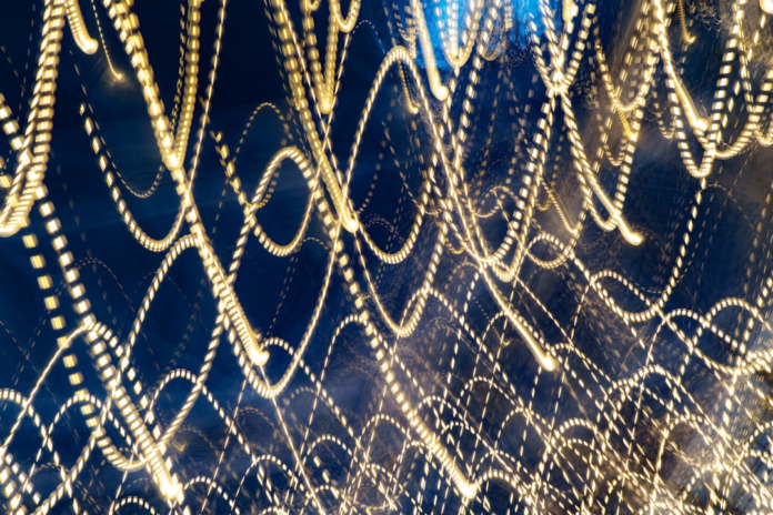 Dynamic golden light trails, resembling intricate data streams or entangled particles, flow through a dark blue, abstract space, conveying complex scientific connection.