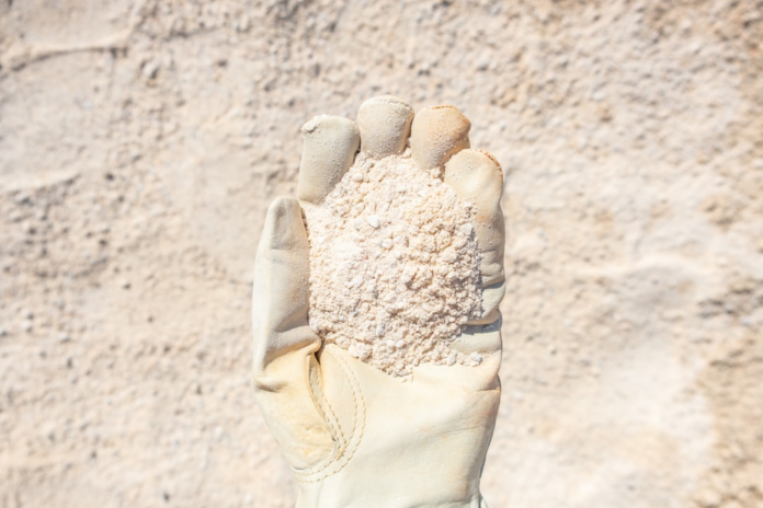 A gloved hand holds a handful of light-colored lunar regolith, foregrounding the vast, dusty surface explored during Apollo missions.