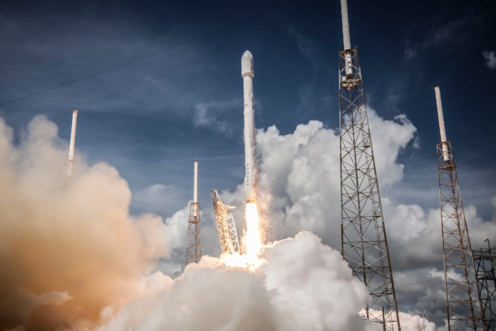 A powerful white rocket launches with a fiery plume and billowing smoke against a dramatic blue sky, surrounded by launch towers, embodying the spirit of space exploration crucial for missions like Artemis.