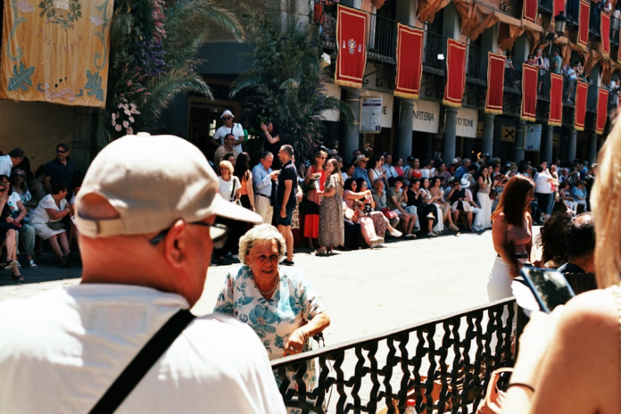 A diverse crowd fills a sunny street adorned with festive red banners, collectively observing an event and illustrating social influence within a large group.