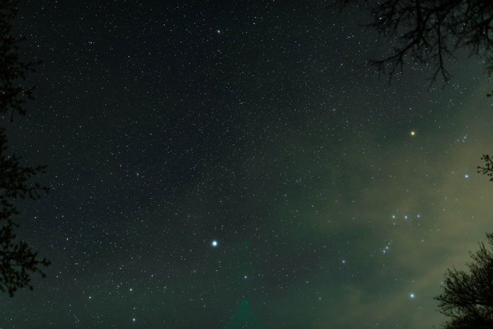 Expansive dark night sky blanketed with countless stars, including visible constellations like Orion, suggesting the vastness and mystery of the universe's origins.