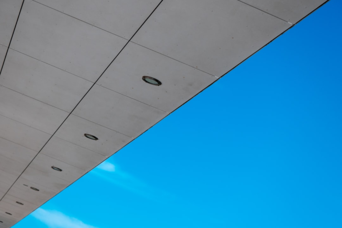 A sleek, gray architectural structure with recessed lights cuts diagonally across a vast, brilliant blue sky, symbolizing the contrasting cosmic fates of universal expansion and contraction.