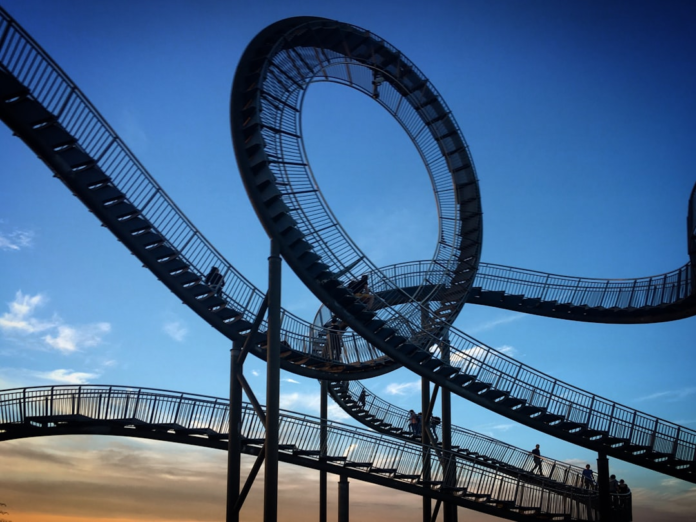 A dramatic, looping elevated walkway with people navigating its intricate paths against a vivid blue and golden sky, symbolizing the complex journey of scientific discovery and protected innovation in biotechnology.