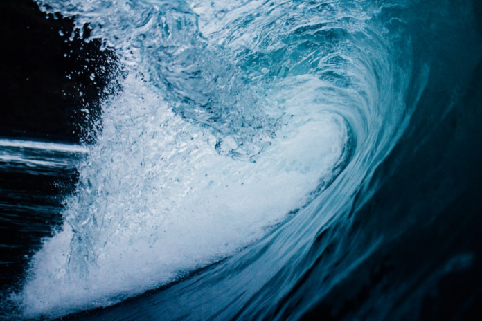 A powerful ocean wave with swirling blue water and crashing white foam illustrates the dynamic forces shaping shorelines.