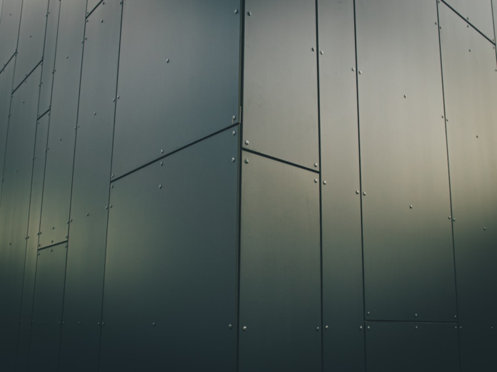 Dark, sleek modern building facade featuring large, flat panels joined by exposed rivets, conveying a precise and structured digital aesthetic.