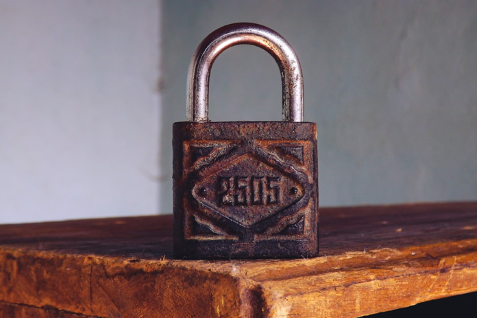 Weathered, rusted padlock featuring the number '2605' on its face, resting on a textured wooden surface, symbolizing strong digital security and essential cyber threat protection.
