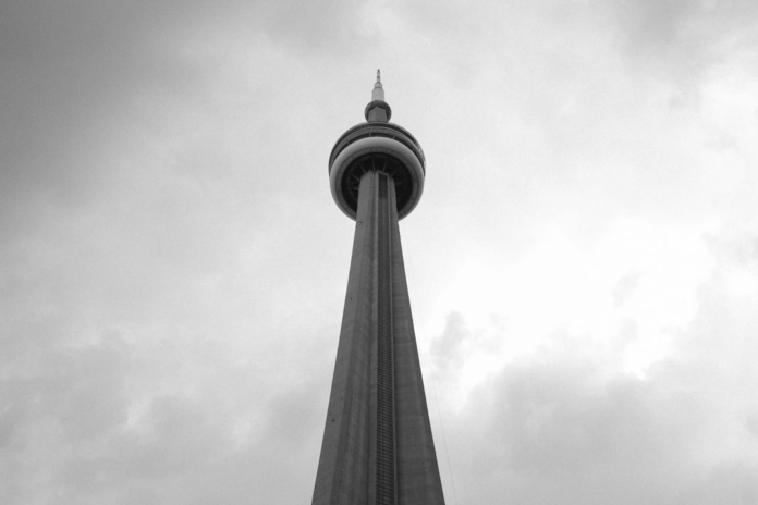 Striking low-angle, black and white view of the CN Tower asserting itself against a vast, cloudy sky, symbolizing the ambitious structures of cosmological theories.