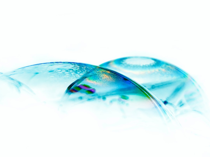 Two luminous, overlapping blue-green spheres exhibit vibrant iridescent light against a pristine white background, abstractly representing atmospheric layers or planetary bodies studied in Earth science.