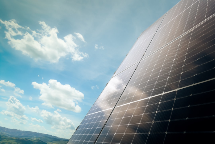 Gleaming solar panels angled towards a bright blue sky with fluffy white clouds, symbolizing sustainable environmental solutions for pollution control.
