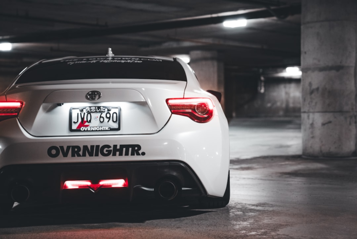 Sleek white sports car with glowing red taillights and custom rear lighting, parked in a dim concrete garage, highlighting the powerful visual presentation of its design.