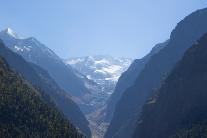 A majestic mountain valley features a massive glacier descending between imposing, rugged peaks under a clear sky, showcasing powerful geological forces and their impact on Earth's landscape.