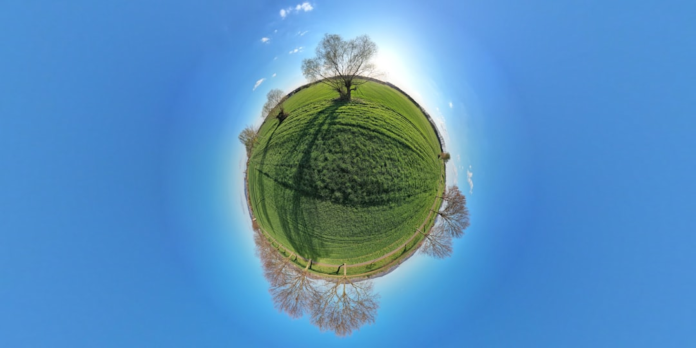 A vibrant green landscape with scattered trees, presented as a miniature planet under a brilliant blue sky, symbolizes the potential for life on a habitable exoplanet like Gliese 581 c.