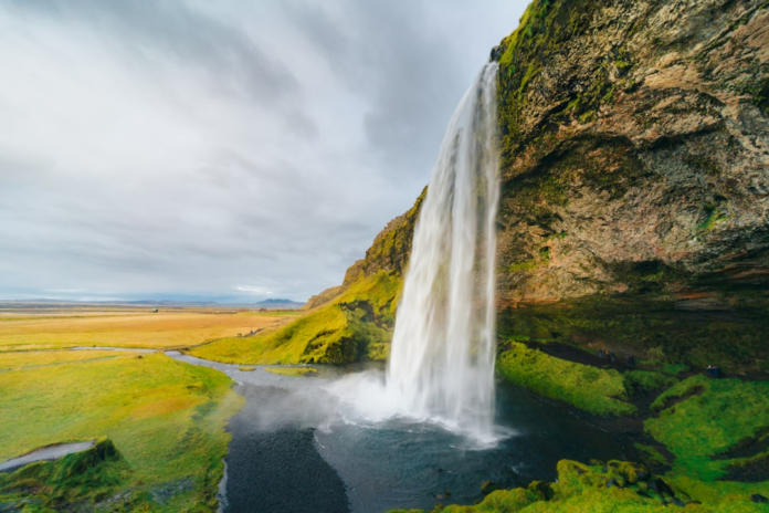 A majestic waterfall dramatically plunges from a towering, moss-covered cliff face into a serene pool, powerfully illustrating the visible flow of groundwater through geological formations amidst a vast, verdant landscape.