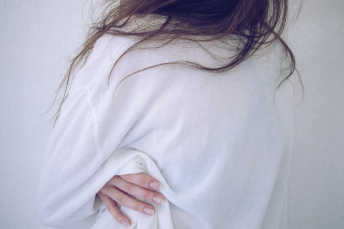 Upper back and hand of a person in a white shirt, with loose brown hair against a light background, highlighting the serene and enduring human form.