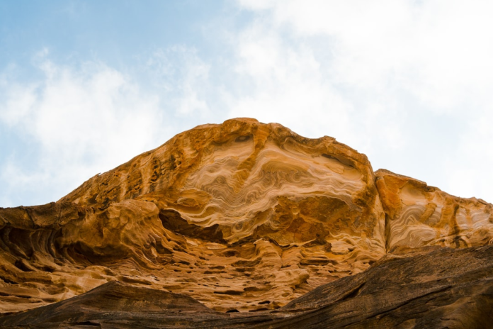 Majestic geological rock formation displaying intricate wavy stratification and erosion patterns in warm earthy tones against a pale sky, illustrating the ancient processes studied in geology courses.