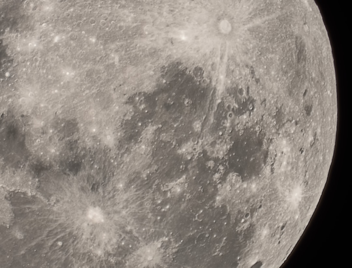 Close-up of the Moon's heavily cratered surface, revealing distinct geological features like bright impact rays and darker mare regions against the deep space.