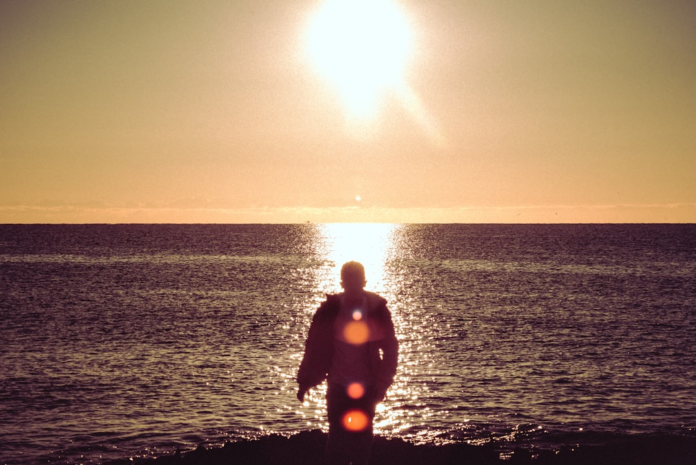 A lone figure is silhouetted against a glowing sunset reflecting on a calm ocean, evoking a sense of powerful energy and the promise of a long, healthy life.