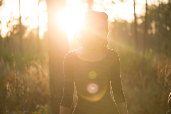A radiant sun completely obscures a person's face as they stand amidst golden foliage, symbolizing the profound secrets and powerful energy of the sun.