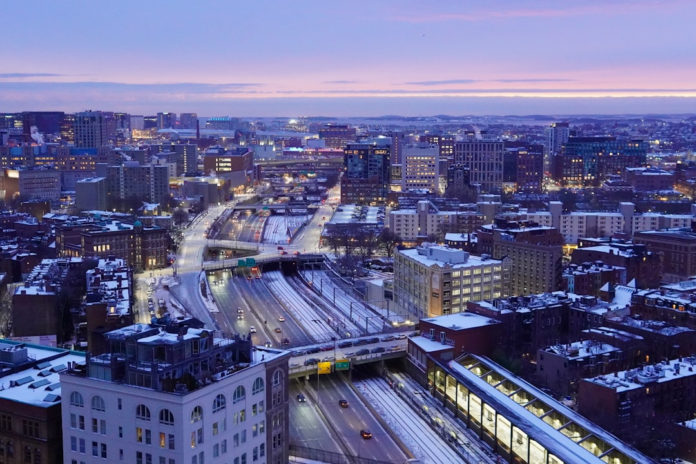 Expansive winter cityscape at twilight, showcasing illuminated highways, active train tracks, and snow-dusted buildings under a vivid purple and pink sky, symbolizing interconnected urban potential.