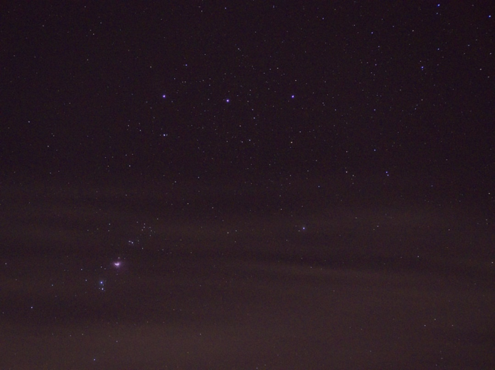 The dark expanse of a starry night sky reveals distant constellations, including the faint glow of the Orion Nebula, embodying the cosmic mystery of life's origins.