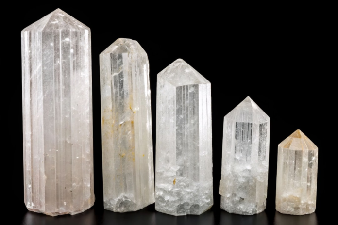 Five translucent columnar mineral crystals, varying in size and clarity, showcase distinct geological forms and faceted structures against a dark background.