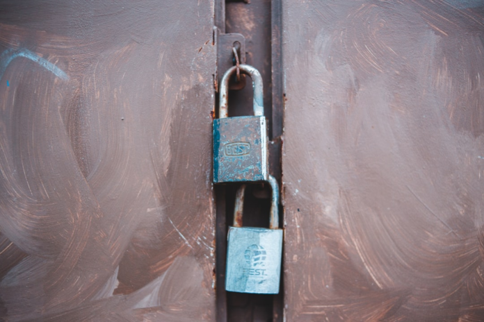 Two weathered padlocks secure a dark, textured metal door, symbolizing strong protection for sensitive personally identifiable information.