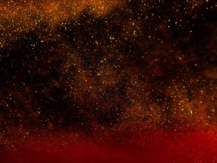 Shimmering golden and red particles against a dark, abstract background, illustrating the mysterious energy and complex nature of the subatomic world in quantum mechanics.
