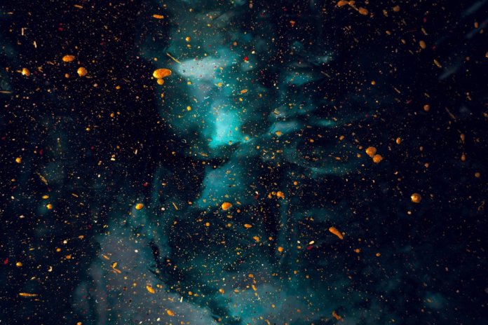 Abstract dark cosmic scene with glowing golden particles and swirling teal nebula, representing the mysterious and vast universe of quantum physics.