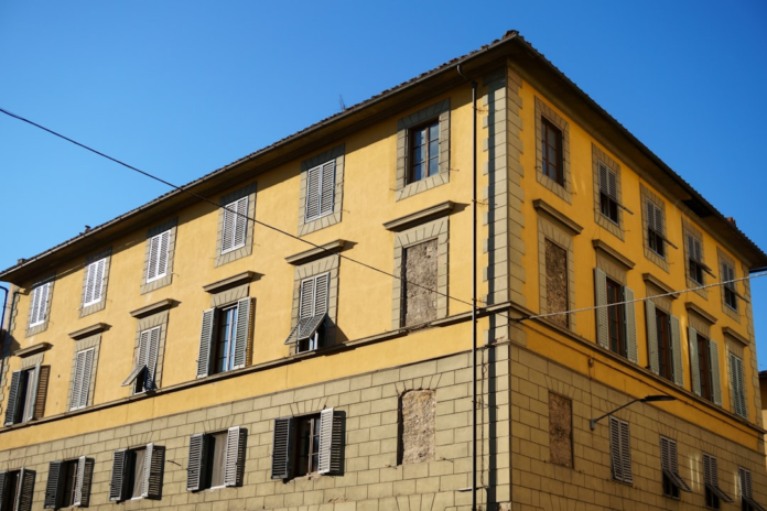 A vibrant yellow historic European building with an array of windows, some open, some shuttered, and some boarded, standing under a bright blue sky, representing diverse inputs that influence perception.