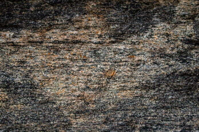 Ancient, layered rock surface showcasing intricate horizontal banding of dark and light mineral grains with subtle reddish-brown hues, reflecting Earth's natural geological assets.