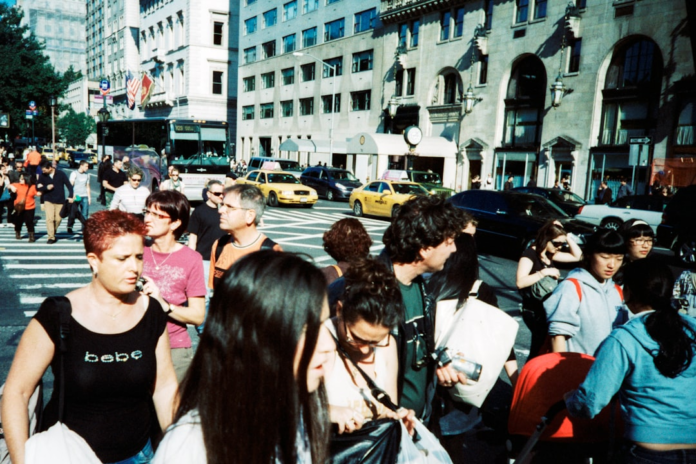 A diverse crowd of pedestrians navigates a bustling city street lined with yellow taxis and classic urban architecture, capturing candid human behavior in a dynamic metropolitan environment.