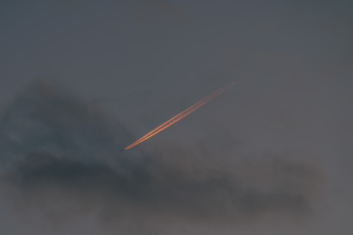 A distant object with a brilliant orange, fiery contrail streaks diagonally across a dark, hazy sky, illustrating the intense heat of atmospheric re-entry.