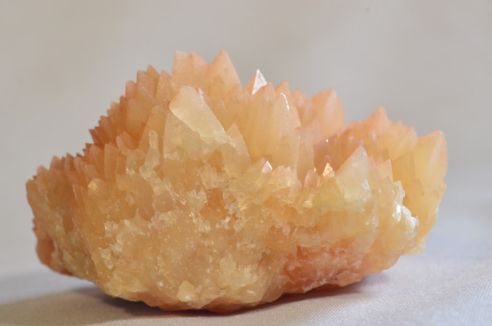 Close-up of a vibrant orange and yellow mineral crystal cluster, featuring sharp, translucent points, representing a geological specimen relevant to supergene enrichment and ore deposits.