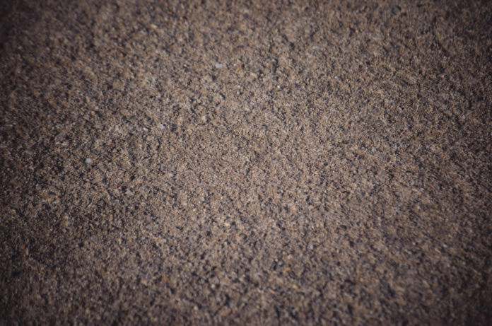 Textured close-up of brown and grey rock fragments and fine sand, representing the granular composition of the Earth's crust.