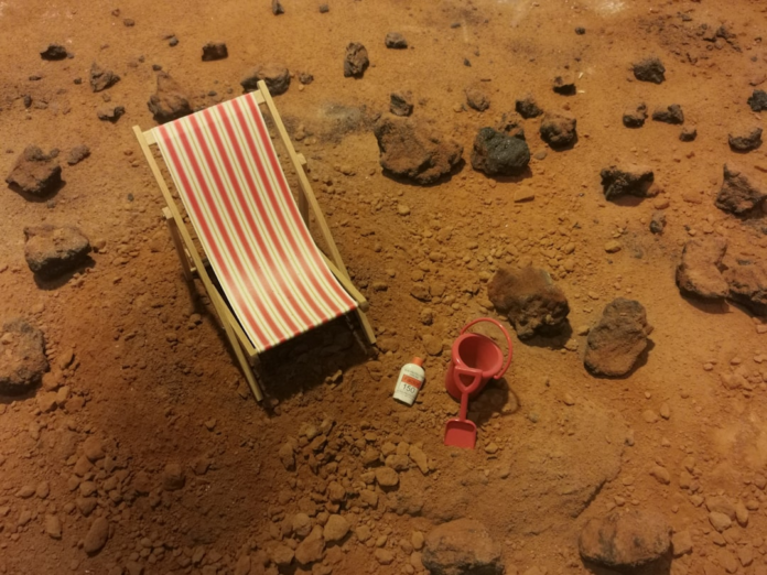 A conceptual image humorously places a striped beach chair, red sand bucket, and sunscreen bottle on a rocky, reddish-brown Mars-like landscape, envisioning future leisure on the red planet for missions like Tianwen-1.