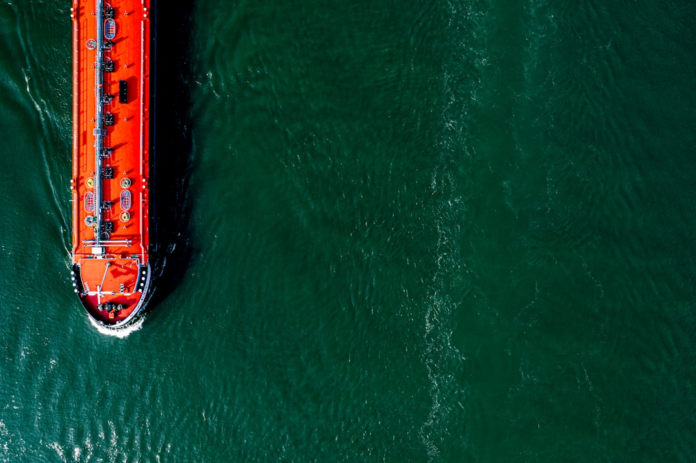 Striking orange maritime cargo vessel moving steadily across expansive dark green water, illustrating the vital flow of global supply chains.