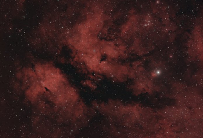 A vast expanse of deep red nebulae interwoven with dark cosmic dust and countless shimmering stars, representing the boundless interstellar medium.